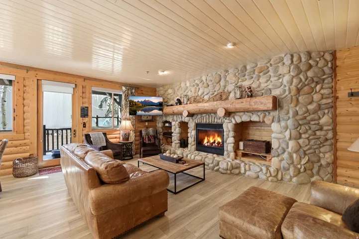 Living area with wood ceiling, a stone fireplace, rustic walls, wood finished floors, and wooden walls