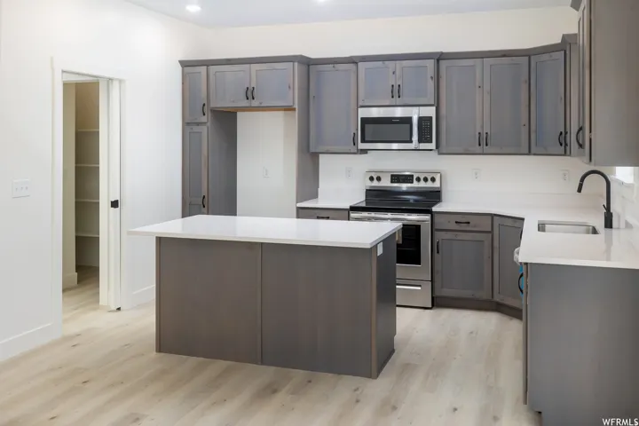 Kitchen with stainless steel appliances, light wood-style flooring, a center island, light stone countertops, and recessed lighting