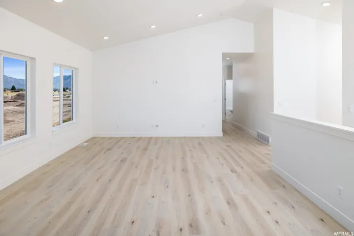 Unfurnished room with lofted ceiling, light wood finished floors, recessed lighting, and a mountain view