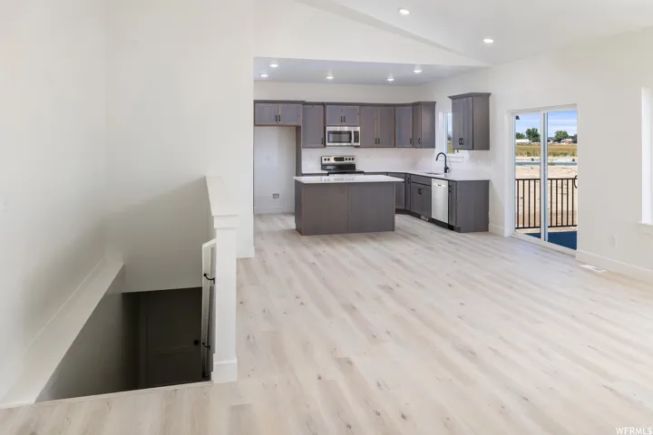Kitchen with a kitchen island, dark wood finish cabinets, light countertops, vaulted ceiling, and light wood-style floors