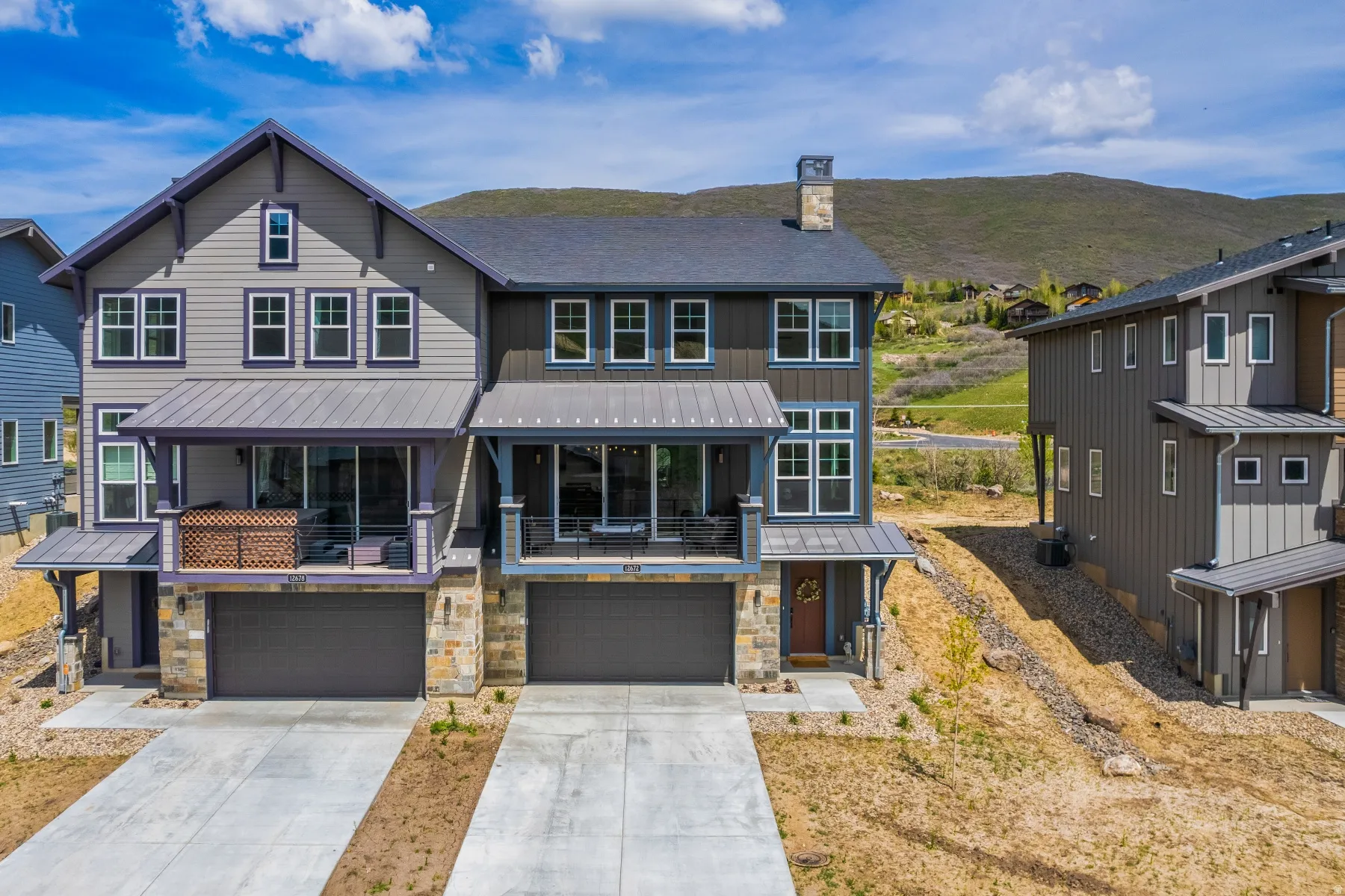 View of front of house featuring driveway, stone siding, a garage, a chimney, and a standing seam roof