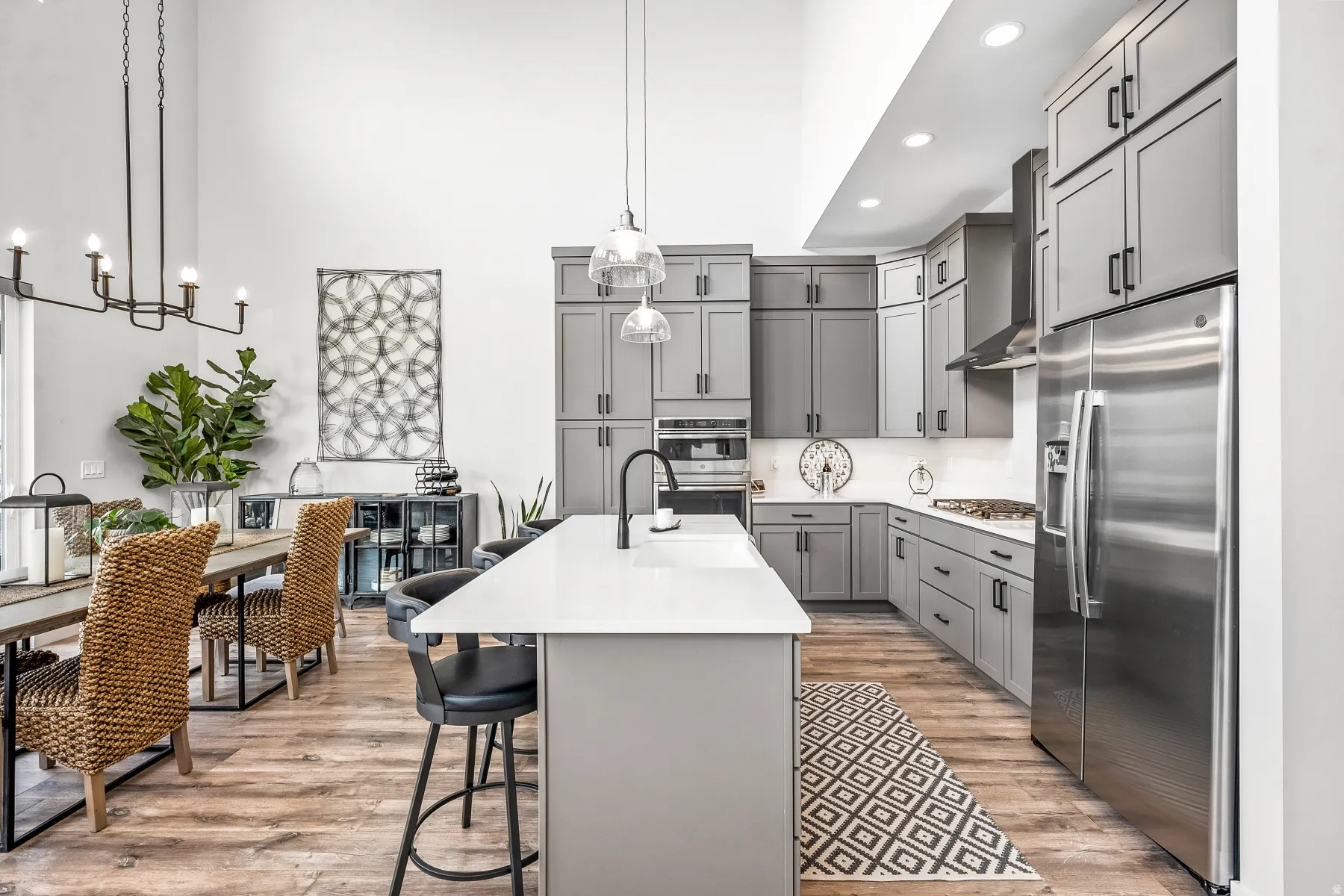 Kitchen featuring gray cabinets, stainless steel appliances, hanging light fixtures, light wood-style flooring, and a high ceiling