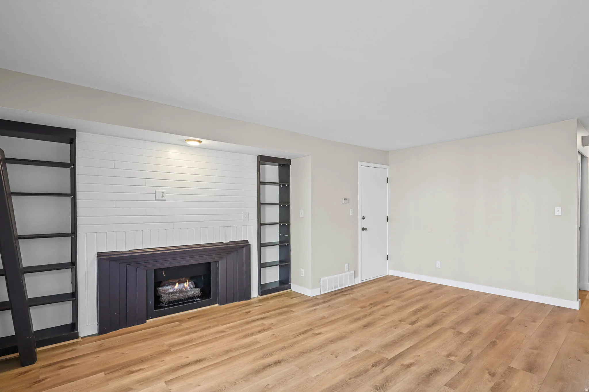 Unfurnished living room featuring light wood-style floors and a warm lit fireplace