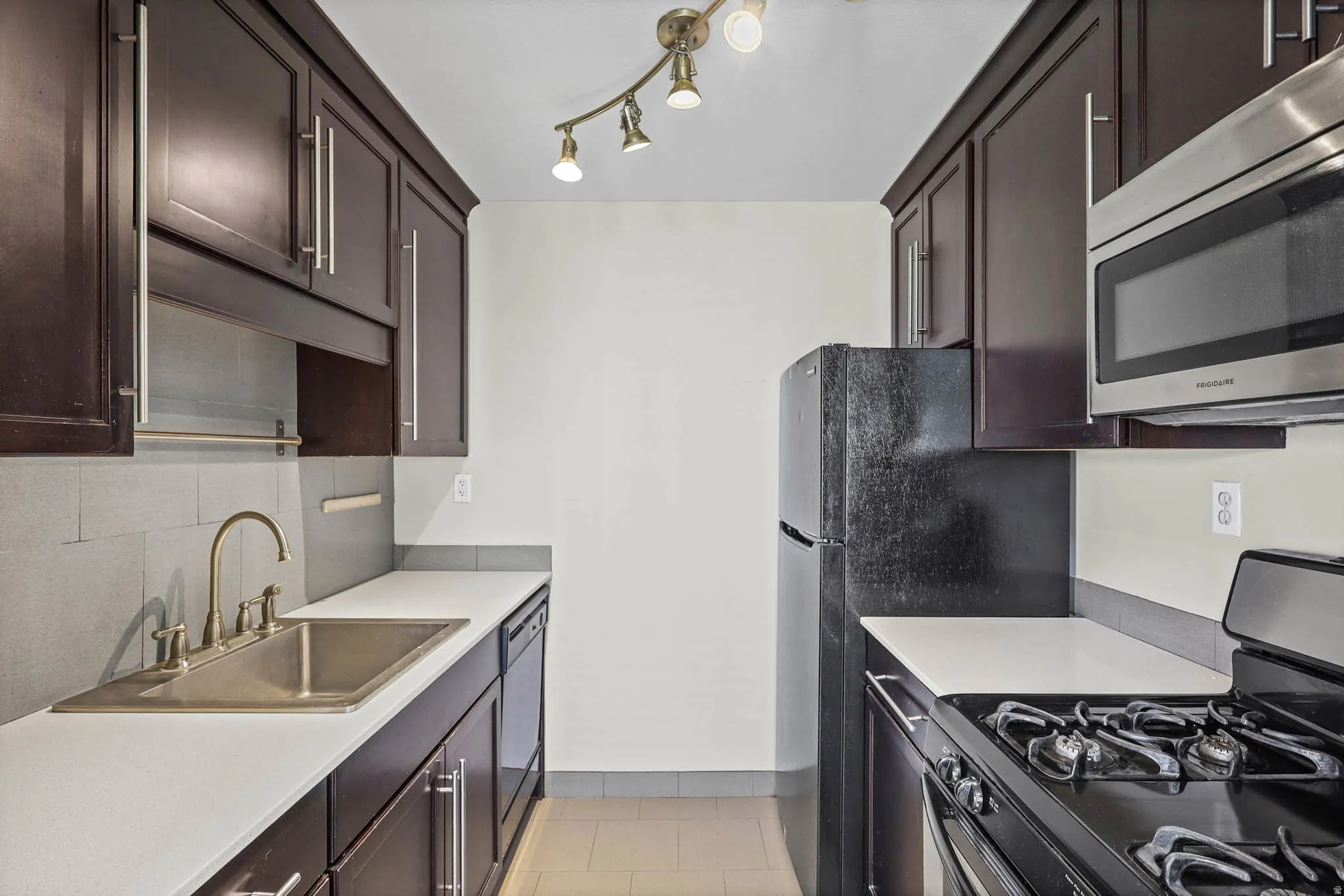 Kitchen with black appliances, dark wood finish cabinetry, and light countertops