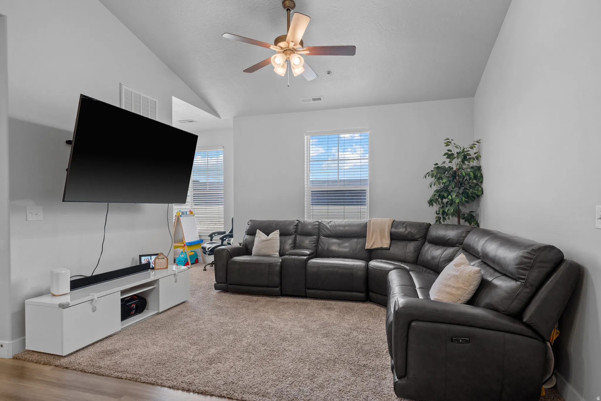 Carpeted living area featuring ceiling fan and vaulted ceiling