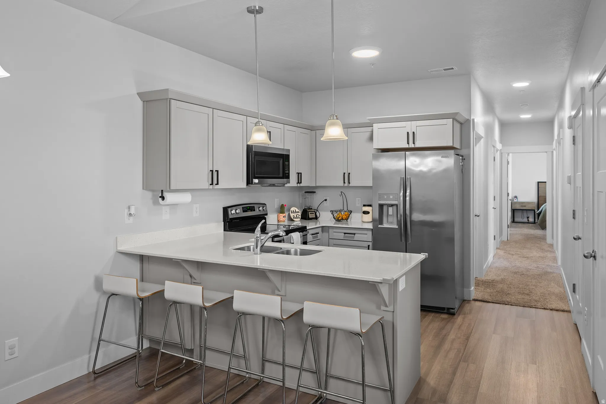 Kitchen with a kitchen bar, a peninsula, stainless steel appliances, light stone counters, and light wood-style flooring