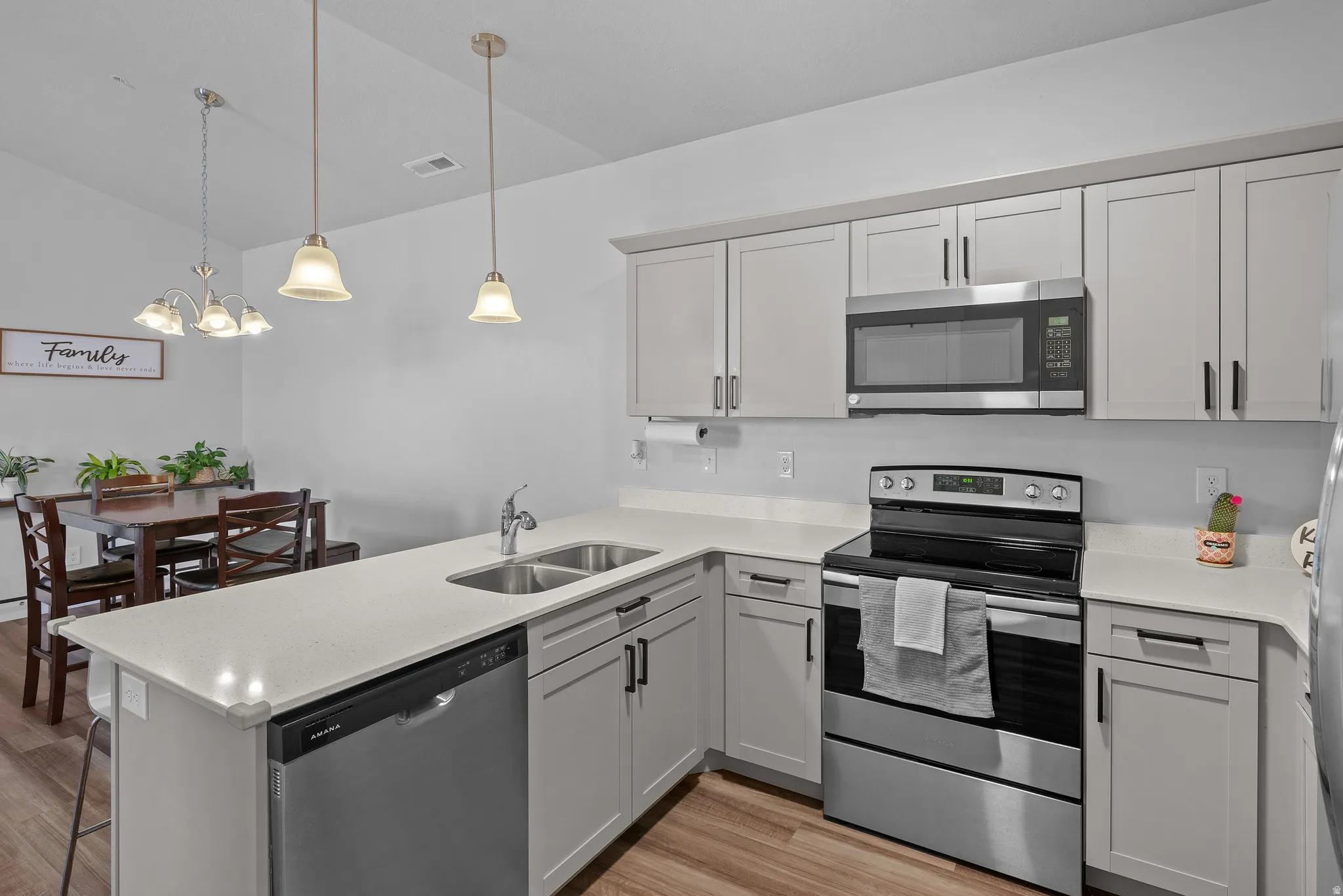 Kitchen featuring stainless steel appliances, a peninsula, light wood finished floors, lofted ceiling, and light stone countertops