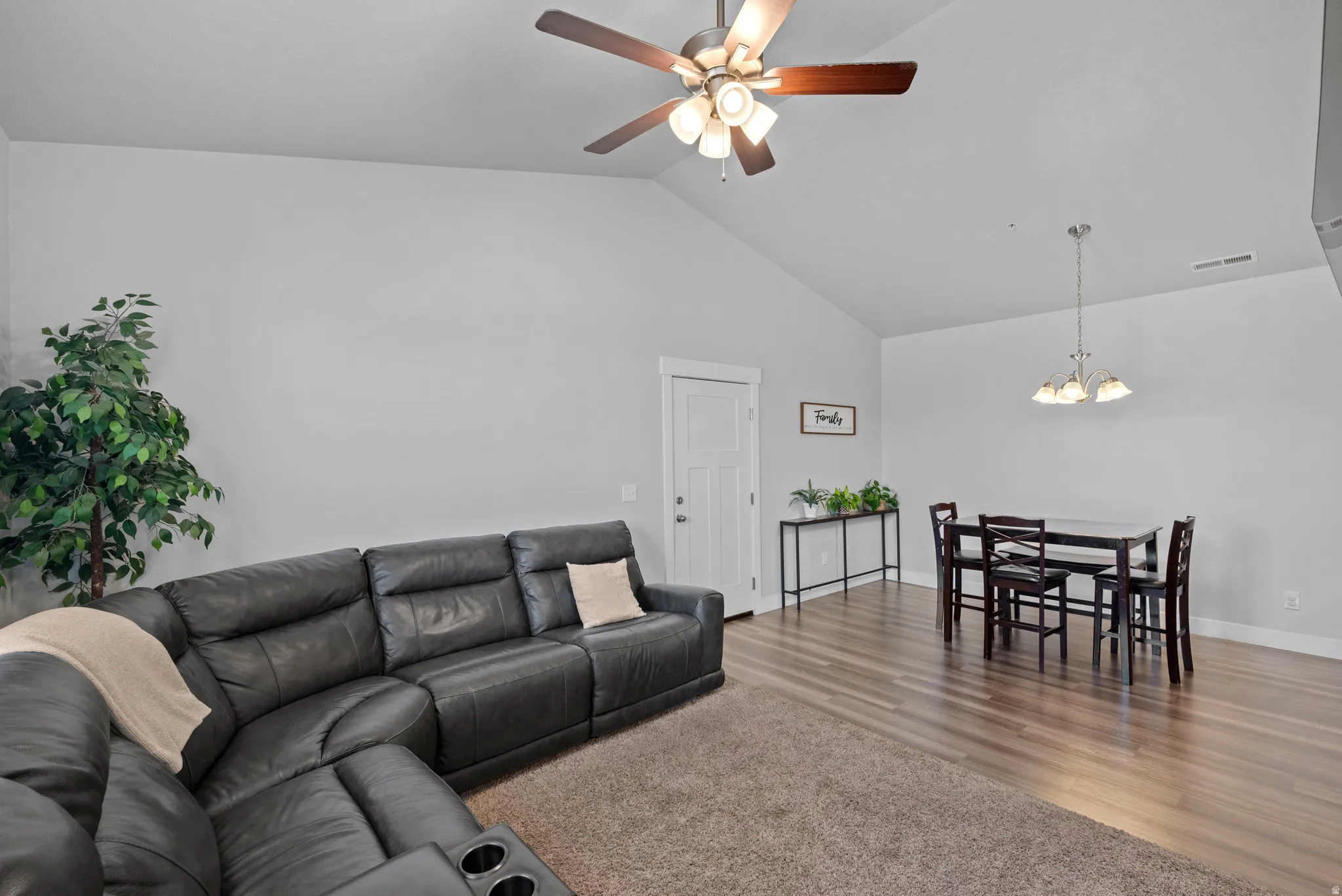 Living room featuring lofted ceiling, suspended lighting, ceiling fan, and wood finished floors