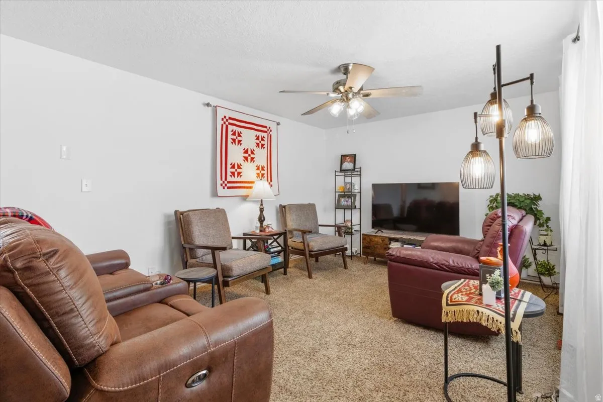 Carpeted living room featuring a ceiling fan and a textured ceiling