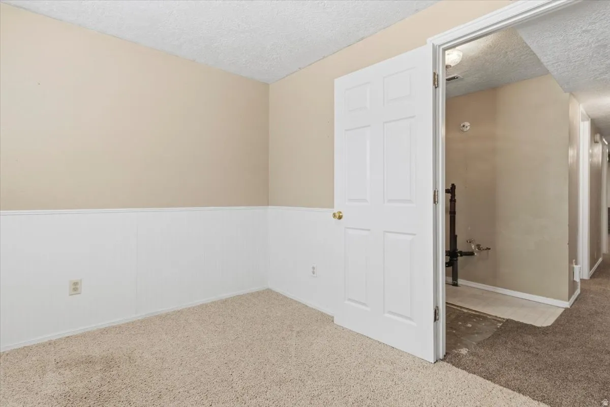 Carpeted empty room with a textured ceiling and wainscoting