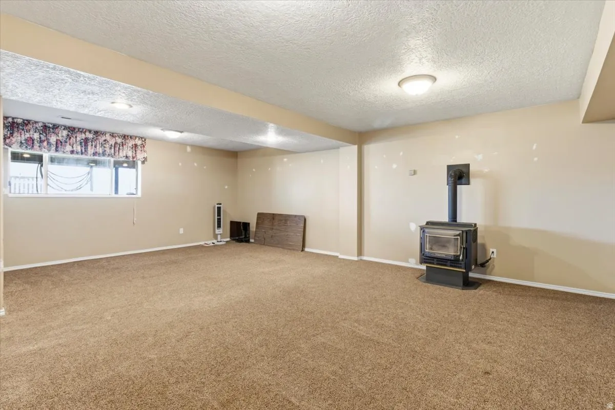 Below grade area with a wood stove, a textured ceiling, and carpet