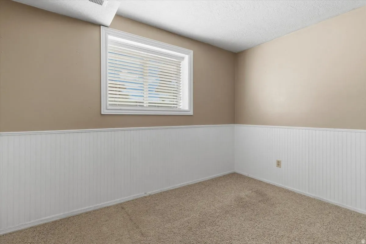 Unfurnished room featuring a textured ceiling, wainscoting, and carpet