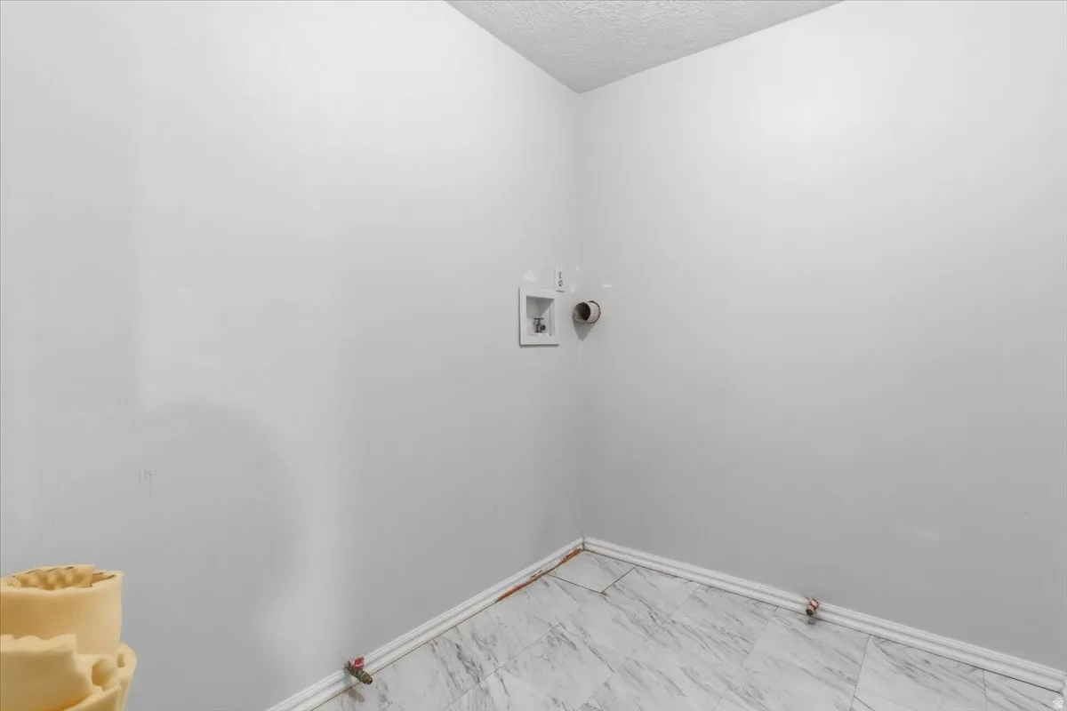 Laundry room with hookup for a gas dryer, a textured ceiling, washer hookup, and light marble finish floors