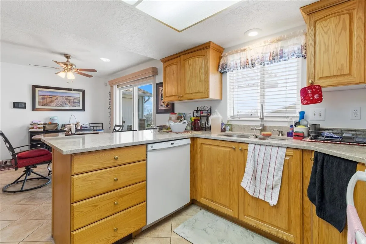 Kitchen with light stone countertops, dishwasher, a peninsula, ceiling fan, and plenty of natural light