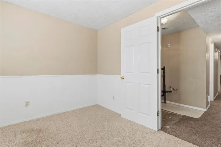 Carpeted empty room with a textured ceiling and wainscoting