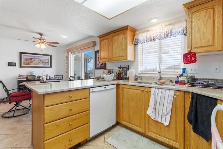 Kitchen with light stone countertops, dishwasher, a peninsula, ceiling fan, and plenty of natural light