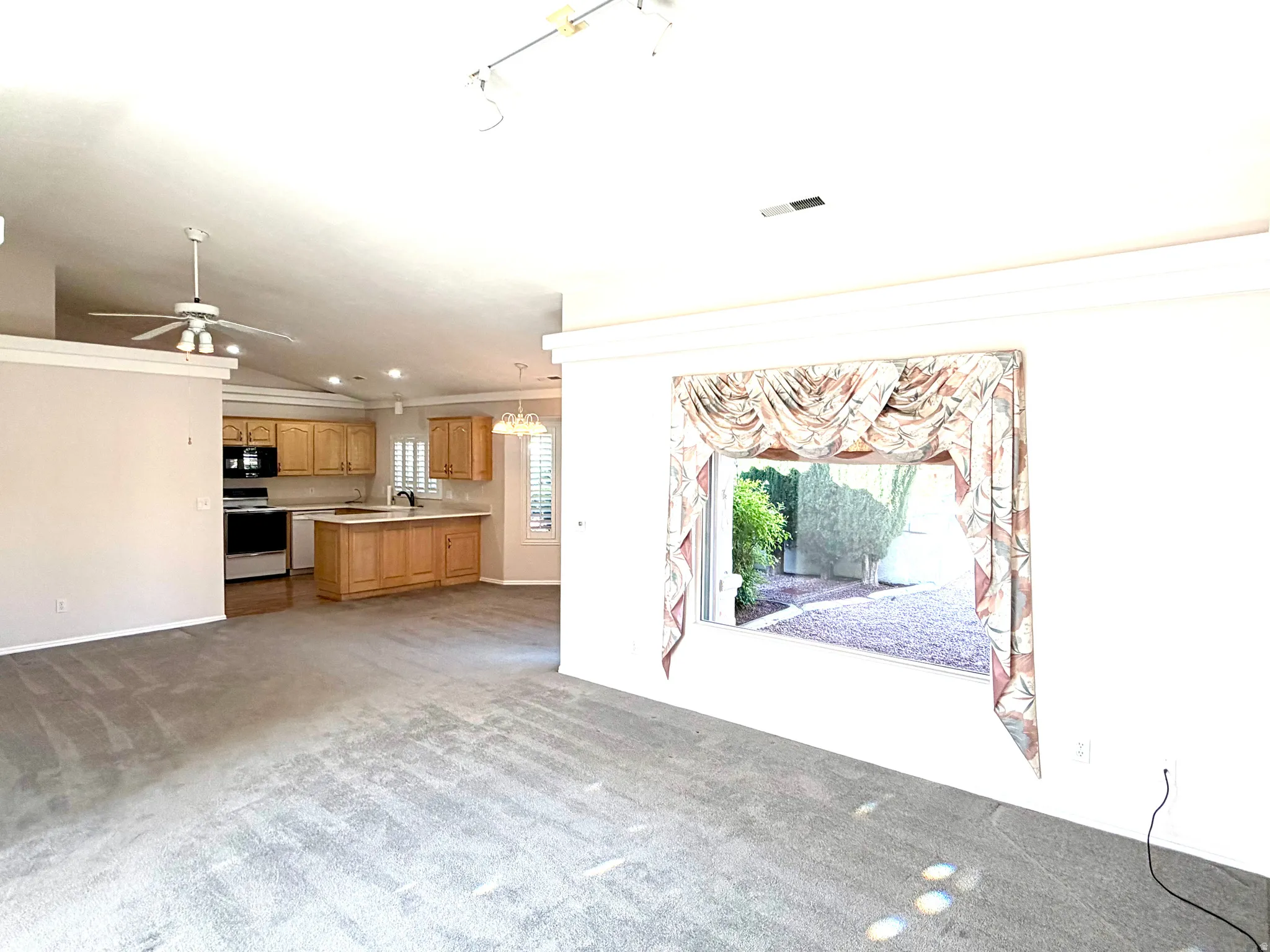 Open-concept living space featuring vaulted ceilings, carpet flooring, and a kitchen with wood cabinetry and an island
