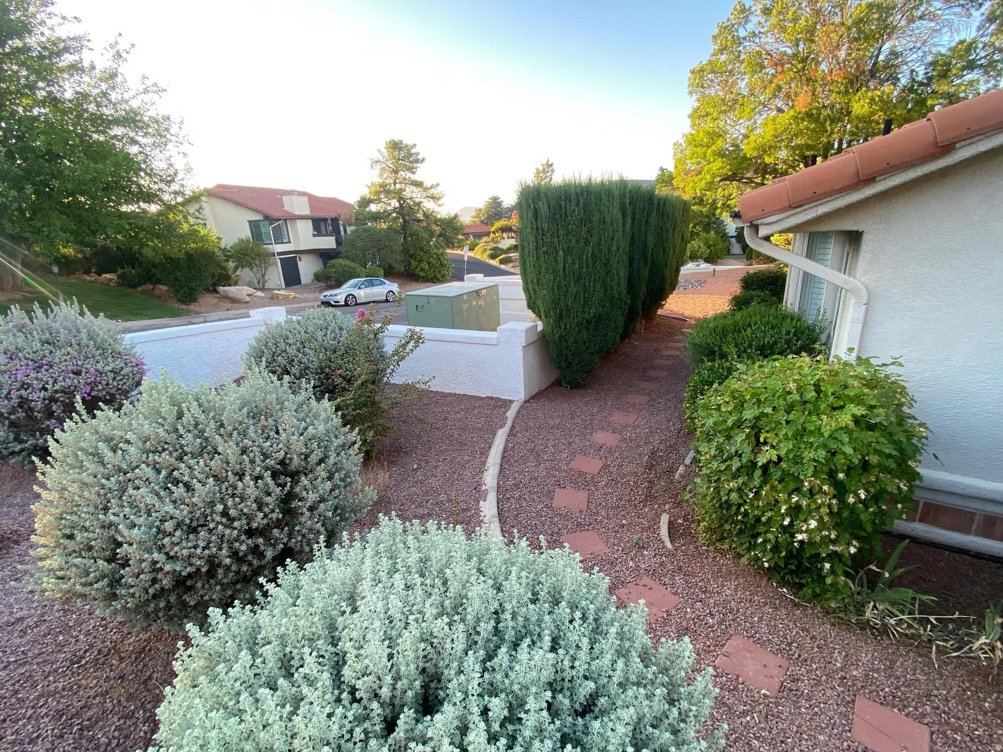 Mature landscaping featuring a winding paver pathway, decorative gravel, and a stucco exterior with a terracotta tile roof