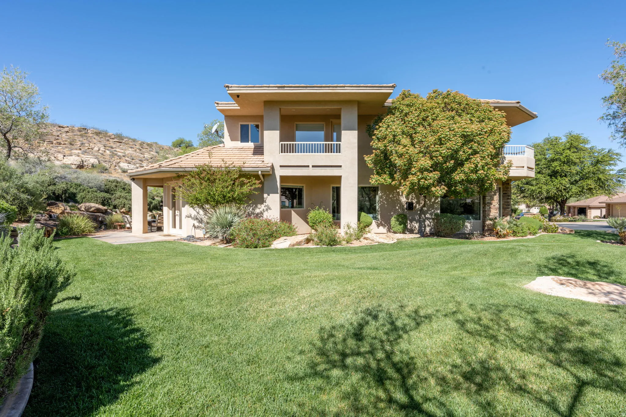 Back of house with a balcony, stucco siding, and a yard