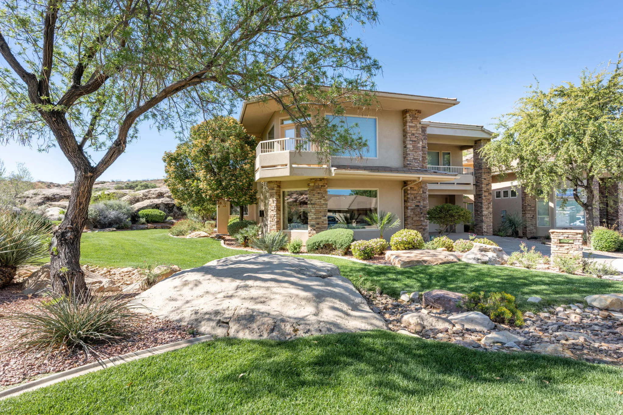 Rear view of house with a balcony, stucco siding, a yard, and stone siding