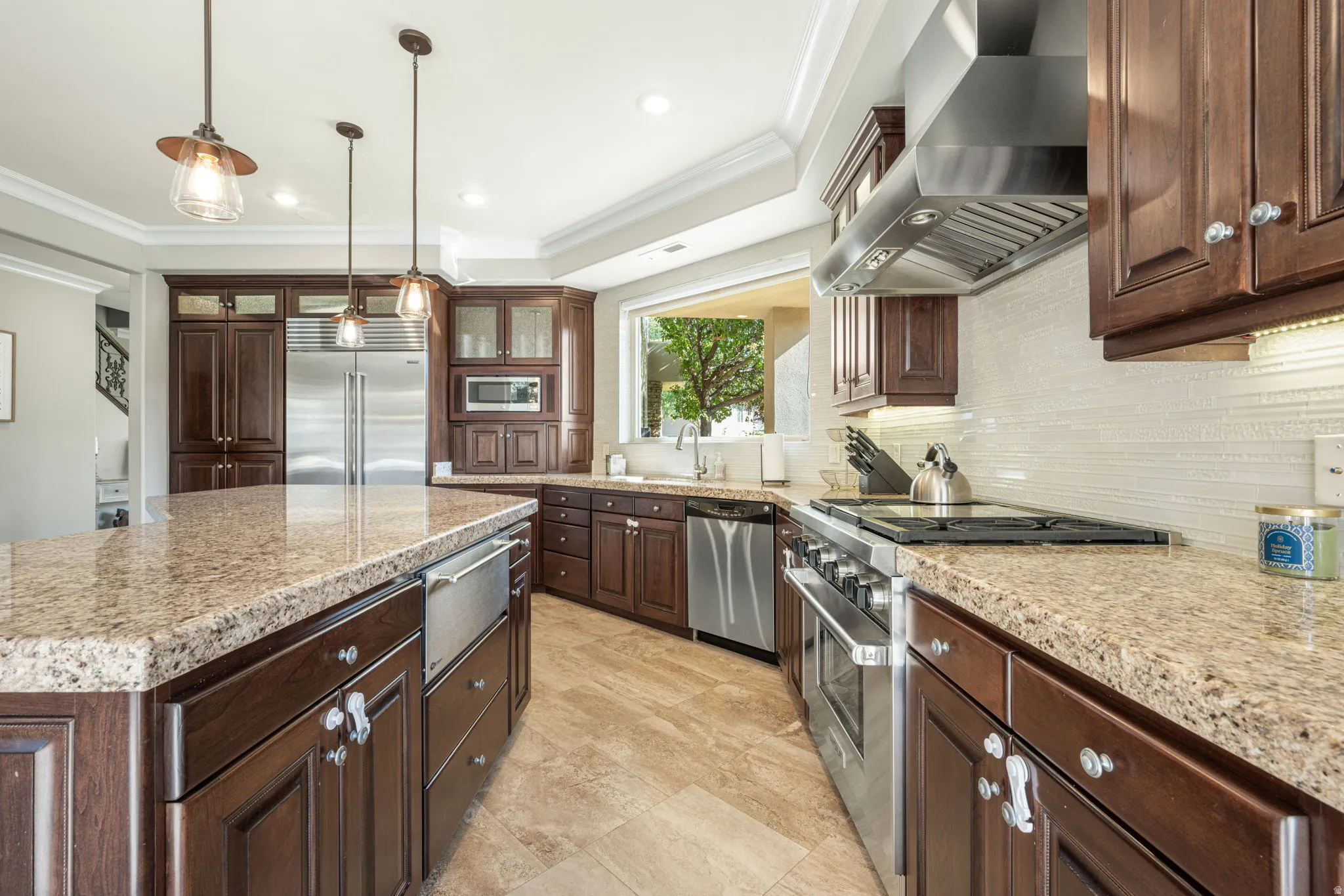 Kitchen with crown molding, built in appliances, decorative light fixtures, light stone countertops, and glass fronted cabinets