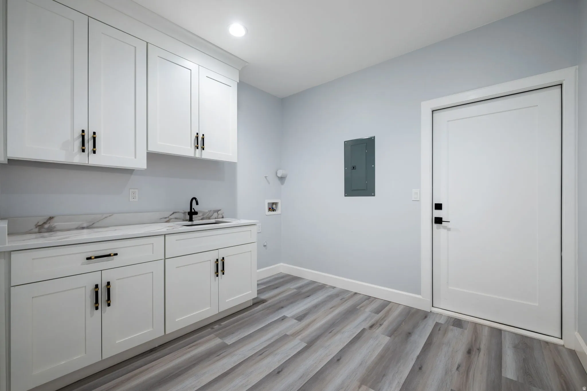 Laundry room with light wood-style flooring, electric panel, cabinet space, hookup for a washing machine, and recessed lighting