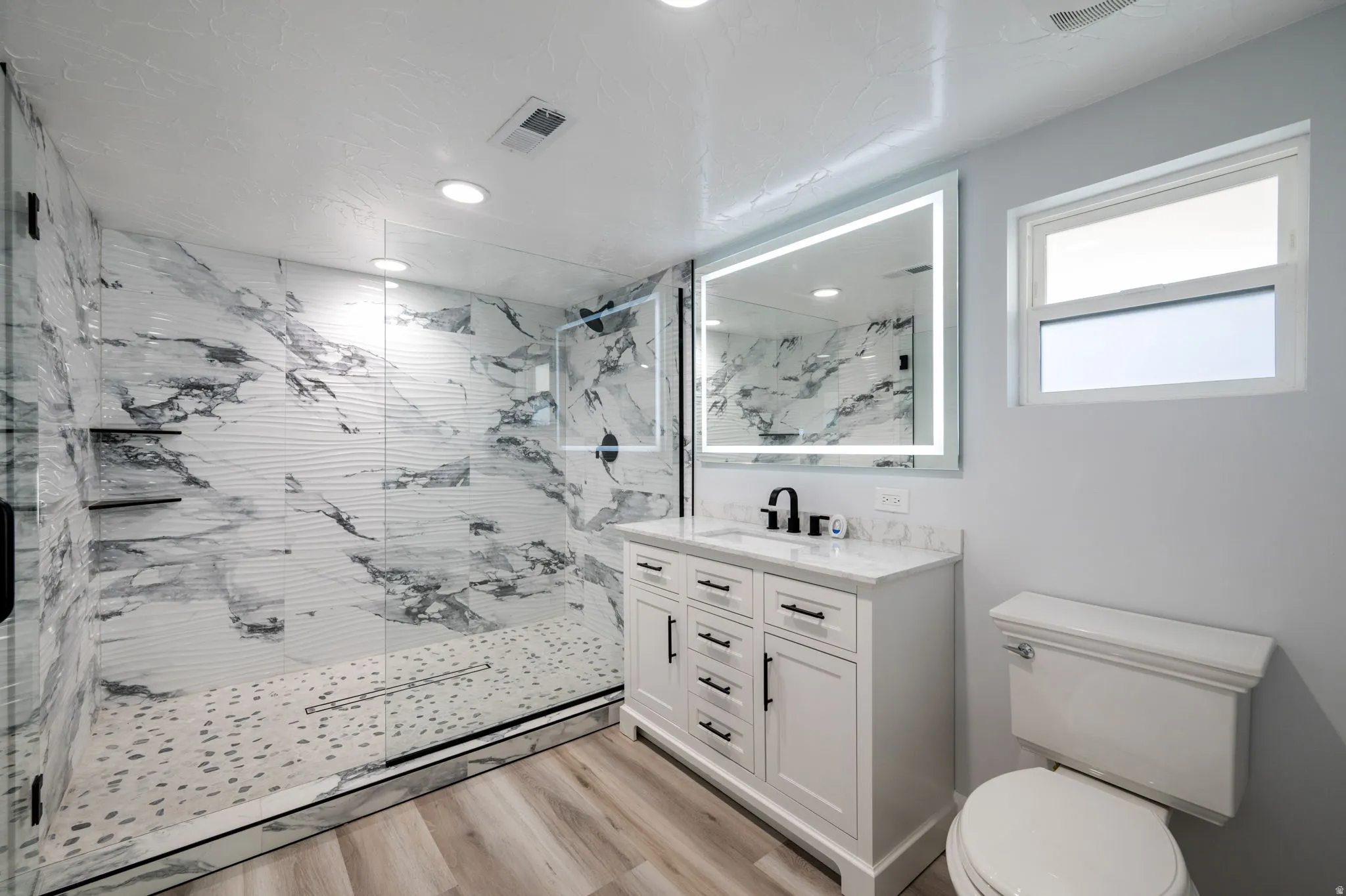 Full bath with a marble finish shower, vanity, light wood-style floors, and recessed lighting