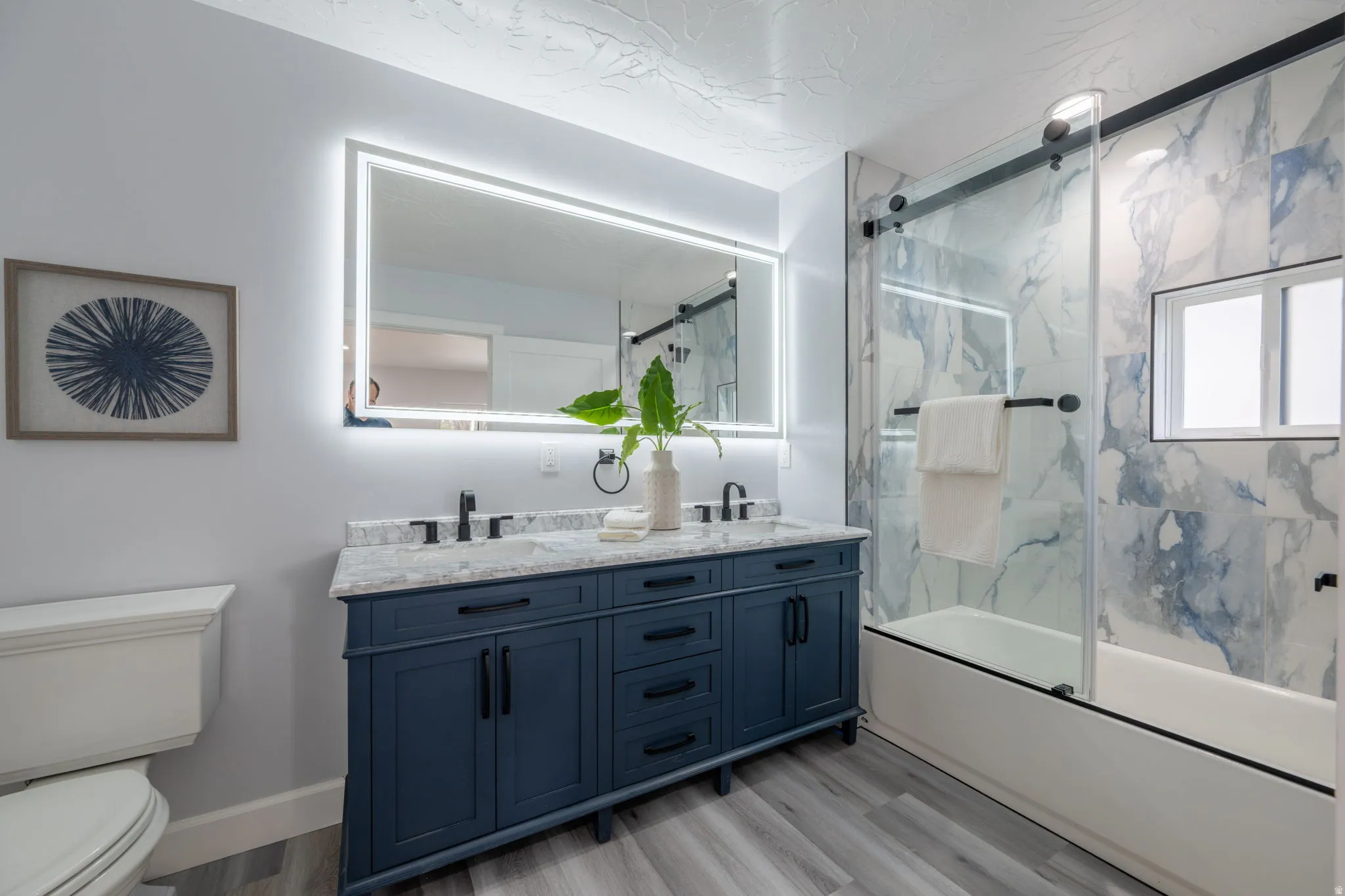 Full bathroom featuring double vanity, light wood-type flooring, and enclosed tub / shower combo