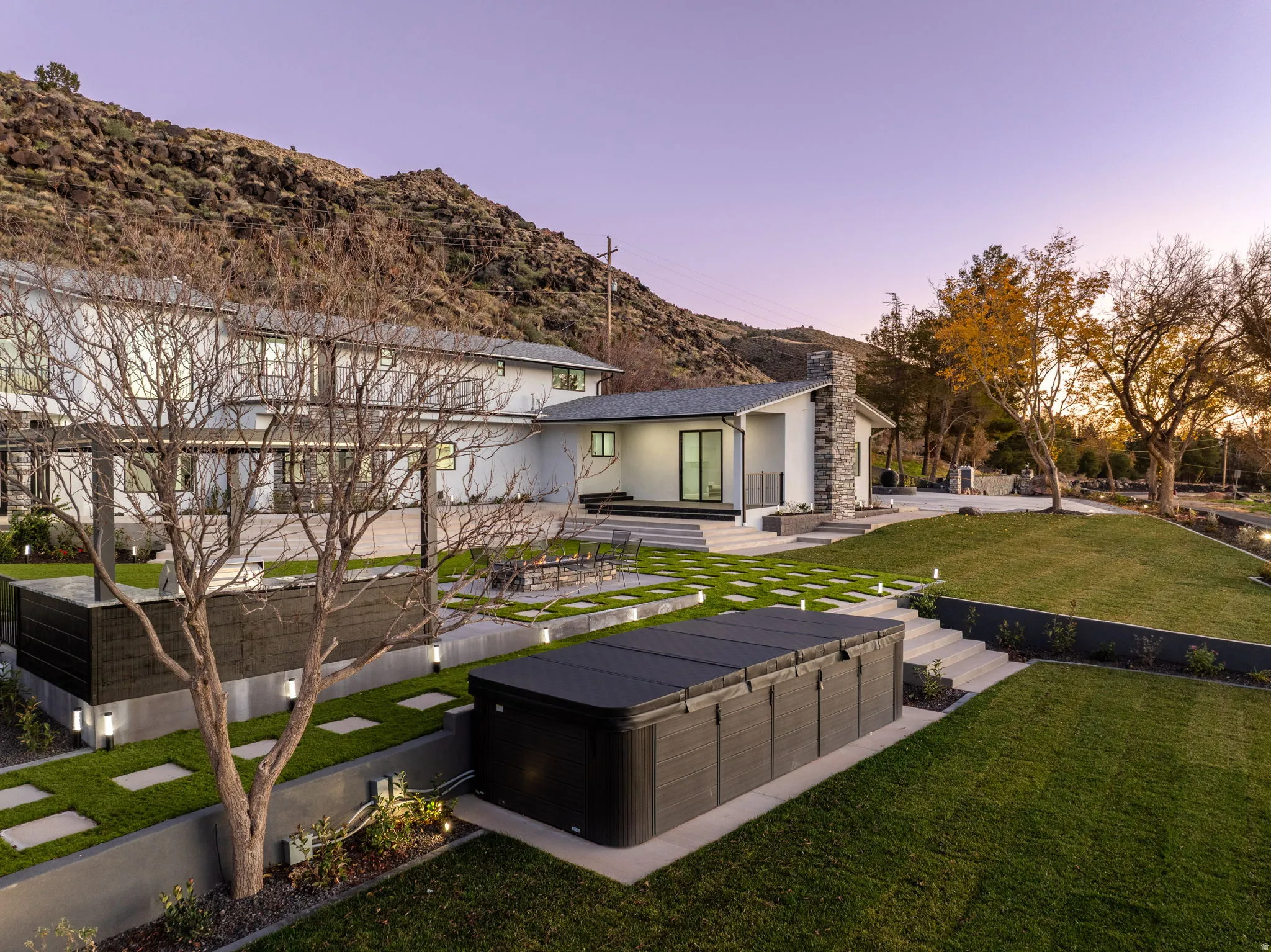 Back of house with a patio area, a lawn, stucco siding, a mountain view, and a hot tub