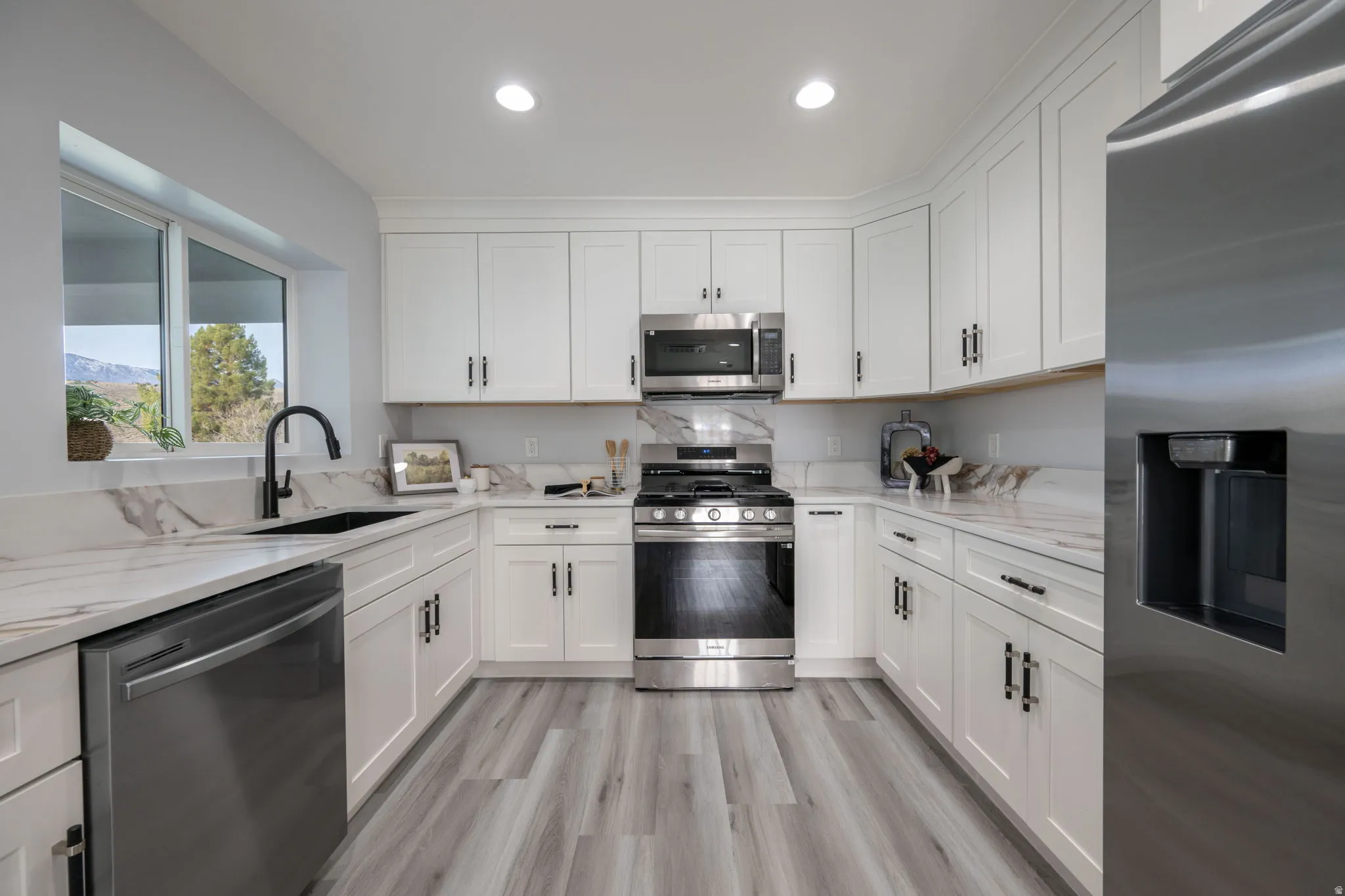 Kitchen featuring stainless steel appliances, white cabinetry, light stone counters, light wood finished floors, and recessed lighting
