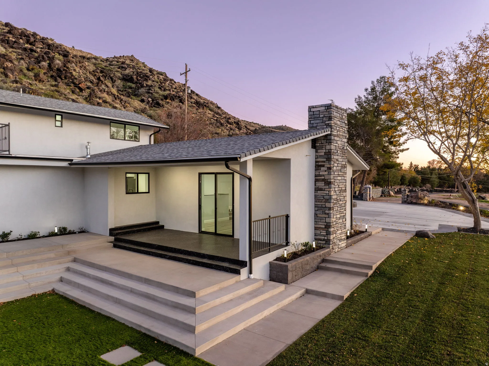 Back of property at dusk with a patio, stucco siding, a yard, roof with shingles, and a mountain view