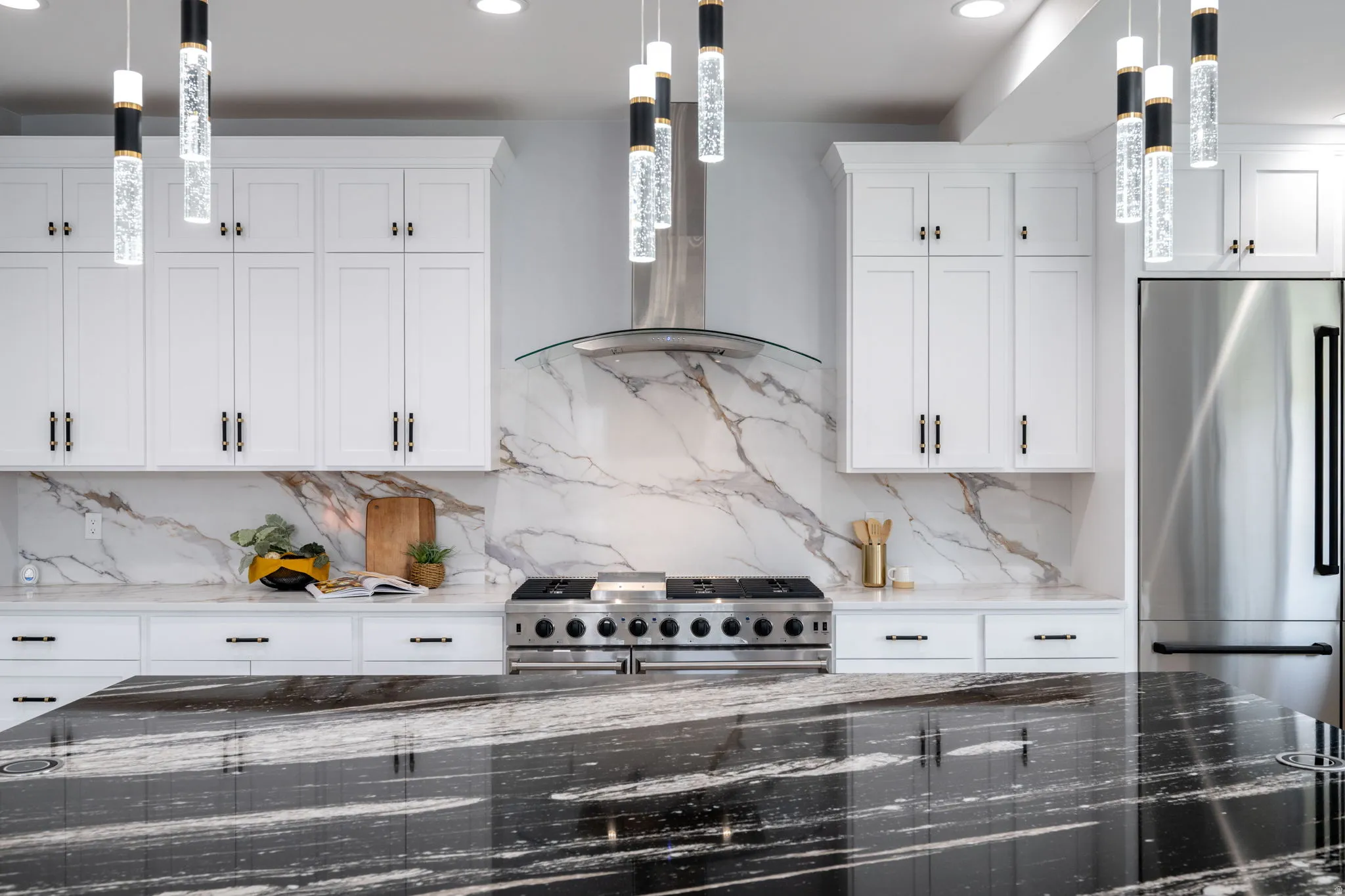 Kitchen featuring dark stone counters, white cabinets, high quality appliances, decorative light fixtures, and decorative backsplash