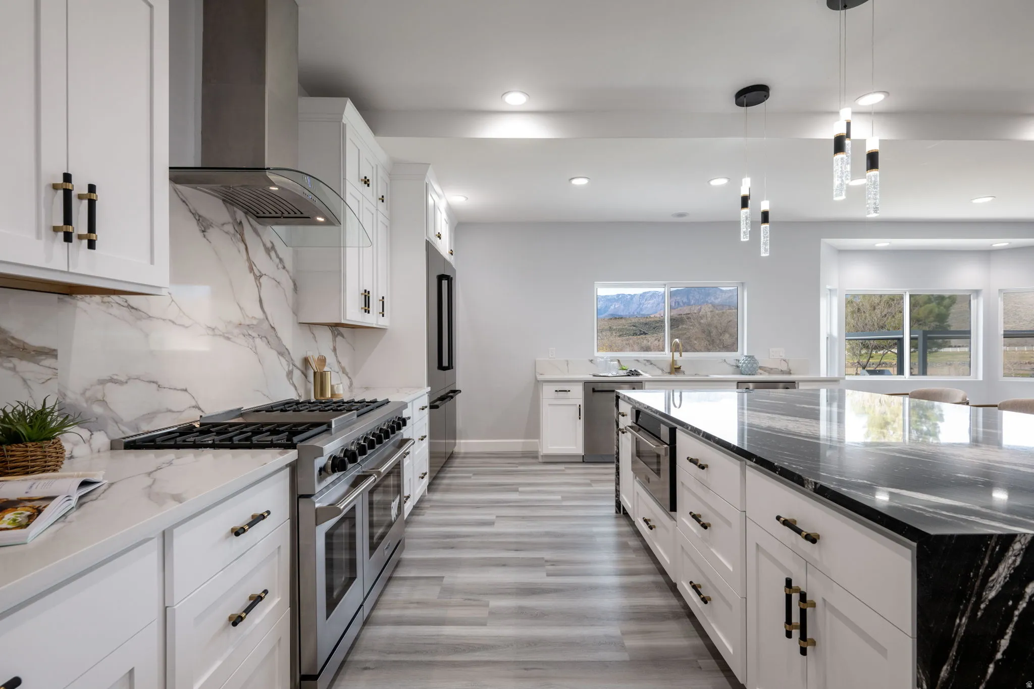 Kitchen featuring dark stone countertops, premium appliances, white cabinetry, and decorative light fixtures