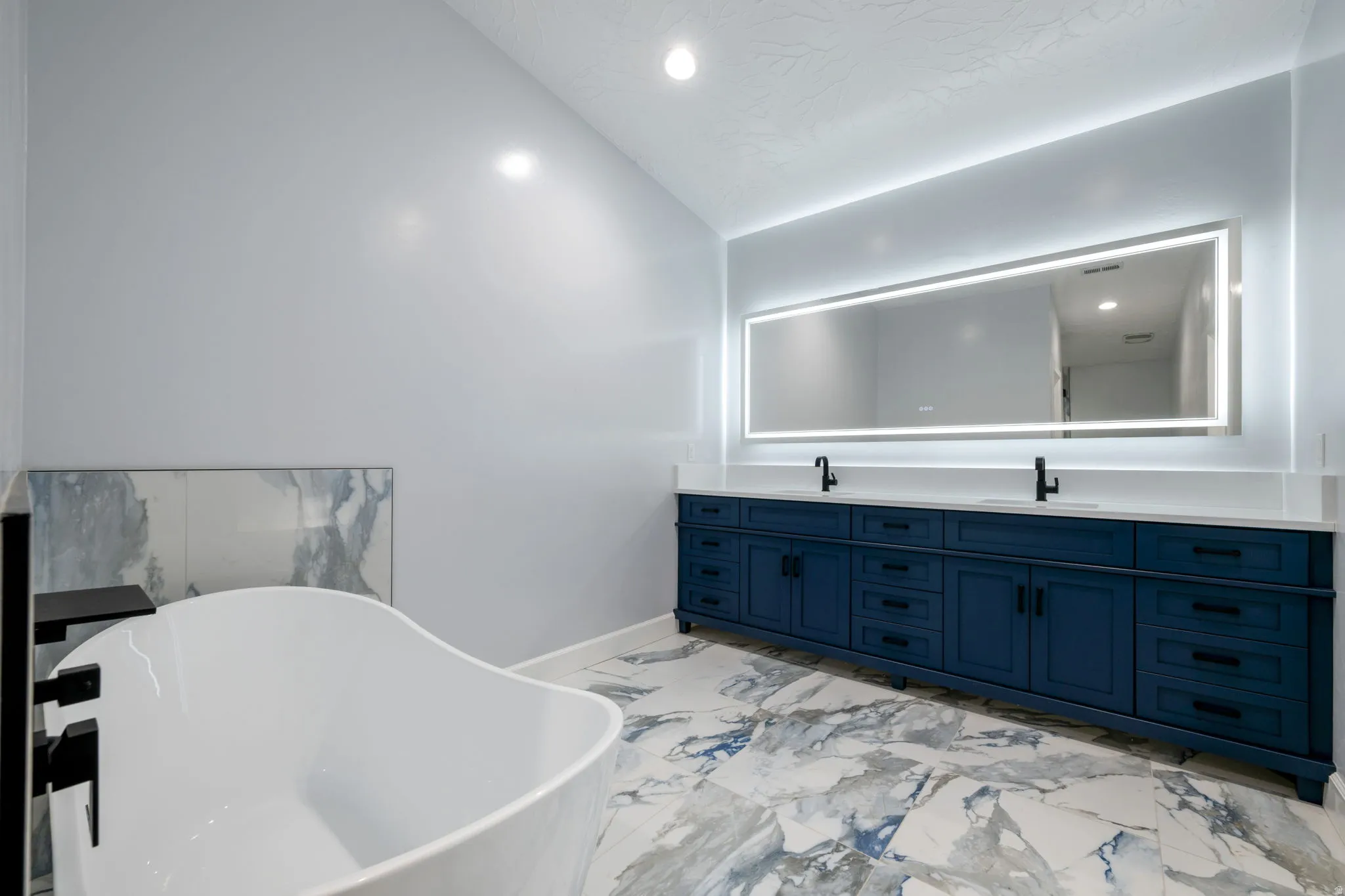 Bathroom featuring double vanity, a freestanding tub, recessed lighting, light marble finish flooring, and vaulted ceiling
