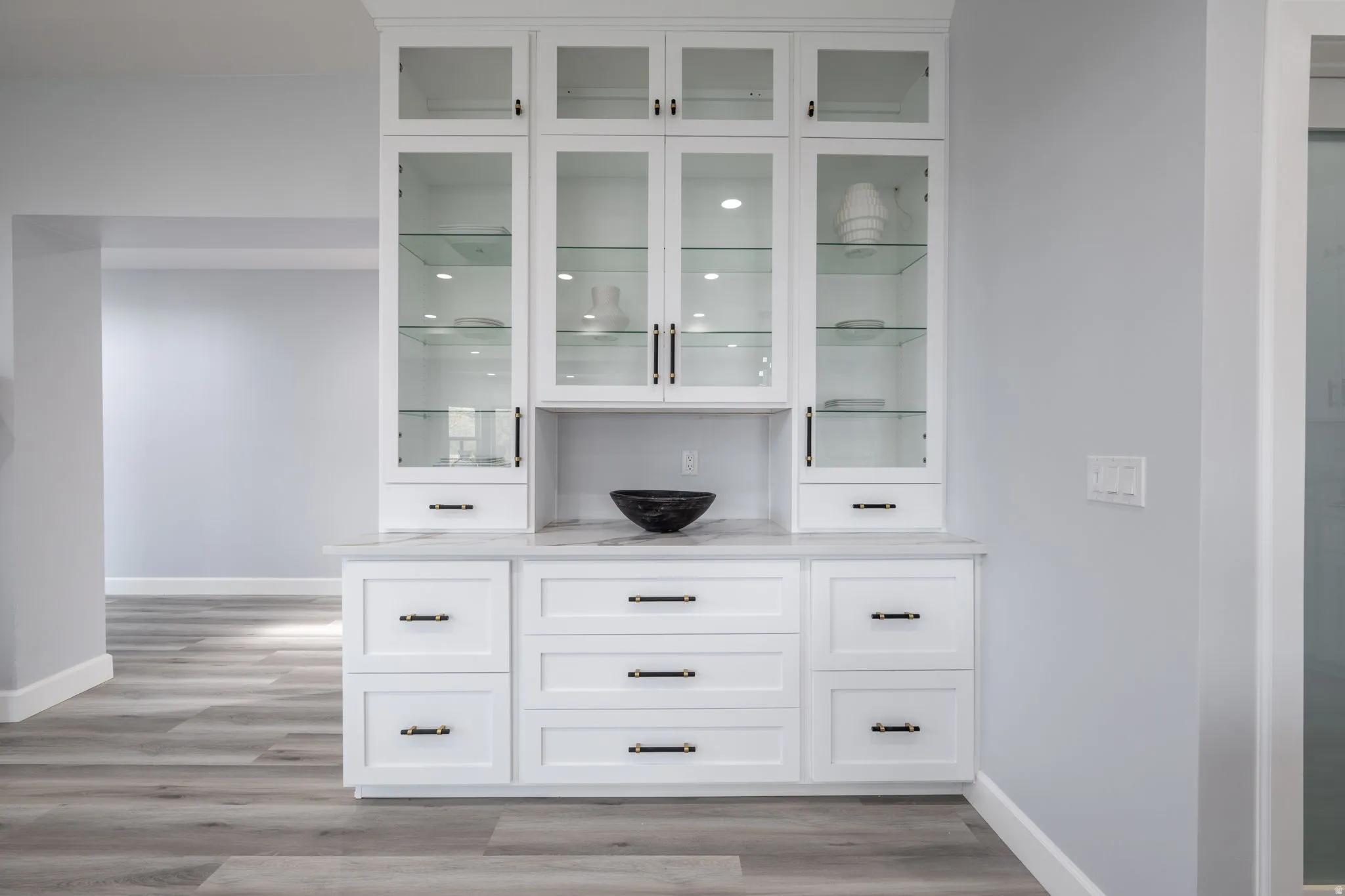 Bar featuring white cabinets, light wood-style floors, and glass fronted cabinets