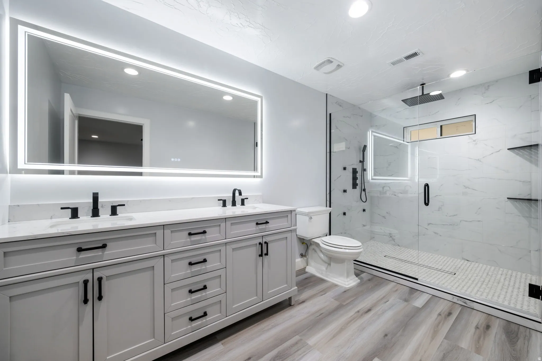Full bath featuring double vanity, light wood finished floors, a marble finish shower, and recessed lighting