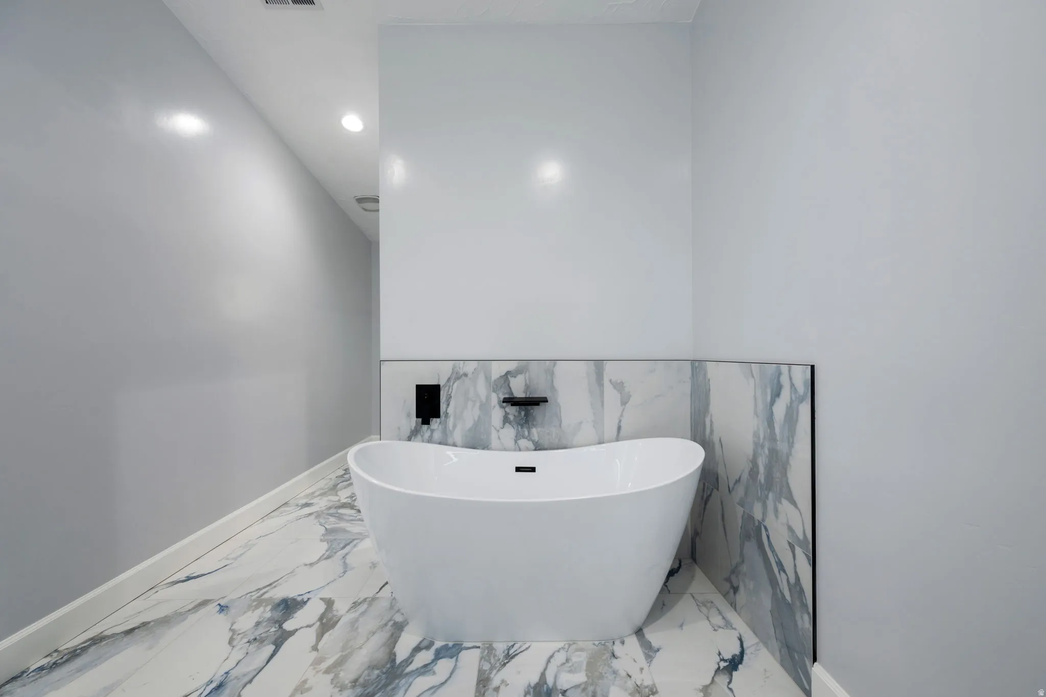 Full bathroom featuring a freestanding tub, recessed lighting, and light marble finish floors
