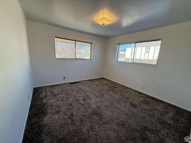 Empty room with dark colored carpet and healthy amount of natural light