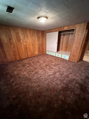 Unfurnished bedroom with carpet floors, wood walls, and a closet
