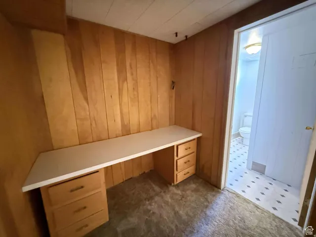 Unfurnished office with built in desk, dark carpet, and wooden walls