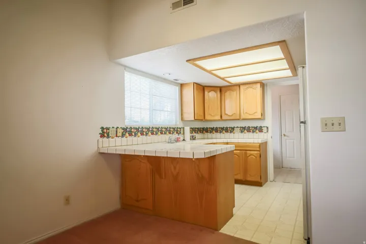 Kitchen with tile counters, a peninsula, light flooring, and a breakfast bar area