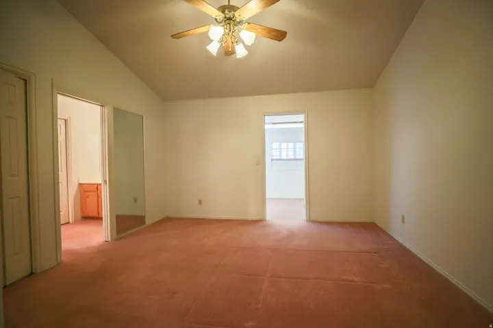 Empty room featuring light colored carpet, ceiling fan, and lofted ceiling