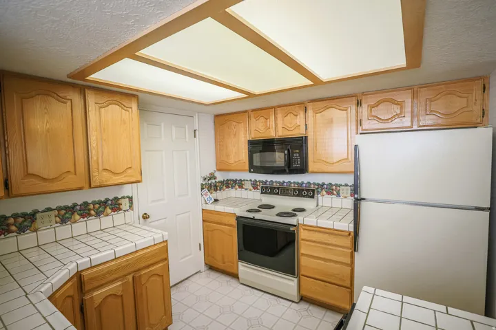 Kitchen featuring tile countertops, freestanding refrigerator, electric range, a textured ceiling, and black microwave