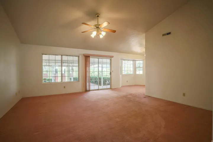 Spare room featuring lofted ceiling, carpet, and a ceiling fan