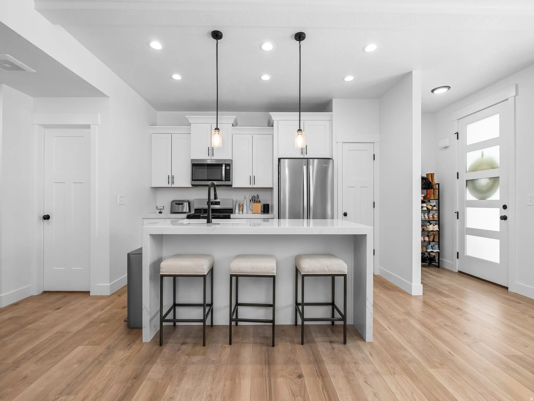 Kitchen with a kitchen island with sink, white cabinets, stainless steel appliances, light stone counters, and decorative light fixtures