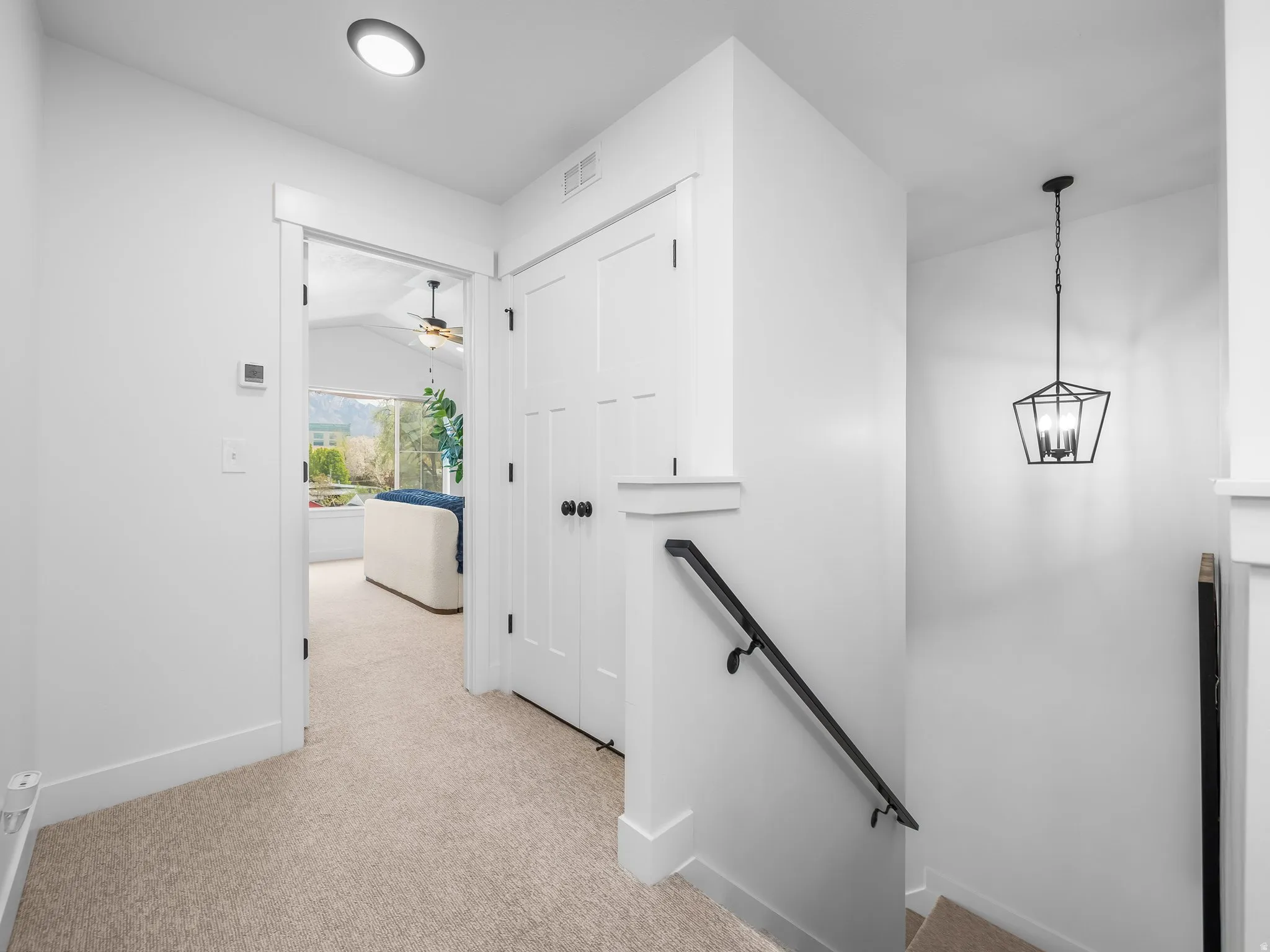 Hallway with an upstairs landing and light colored carpet