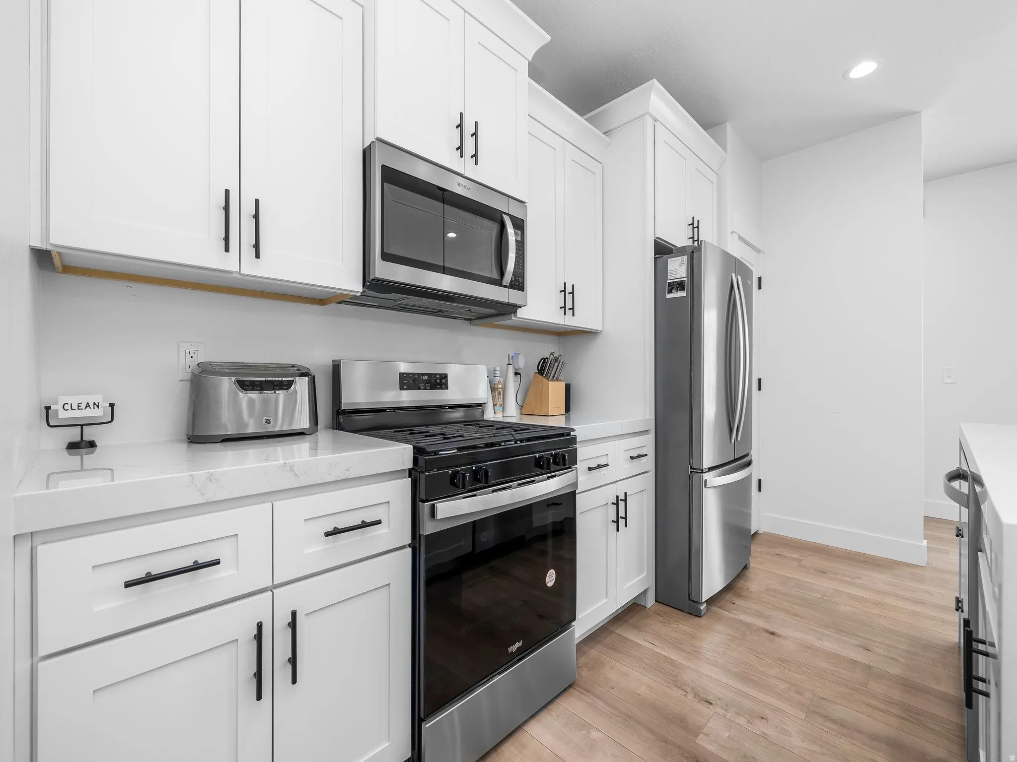 Kitchen with stainless steel appliances, light wood-style flooring, white cabinets, light stone countertops, and recessed lighting