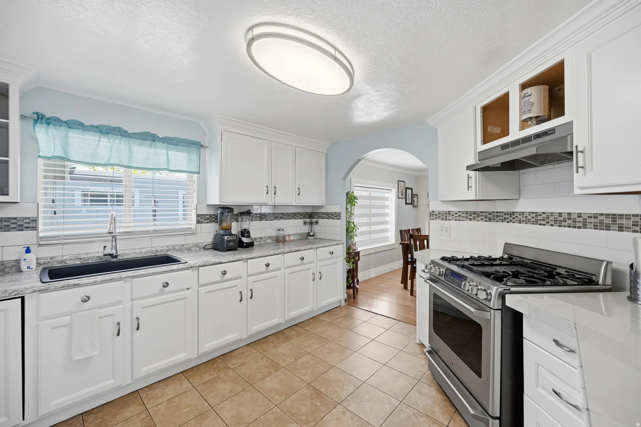 Kitchen featuring stainless steel gas range oven, white cabinetry, arched walkways, and a textured ceiling