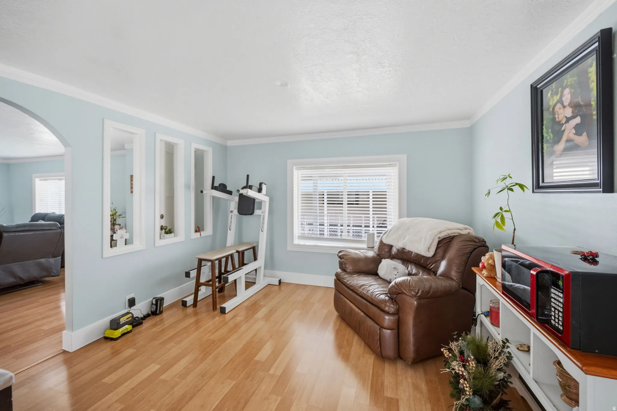 Sitting room with arched walkways, light wood-style floors, crown molding, and a textured ceiling