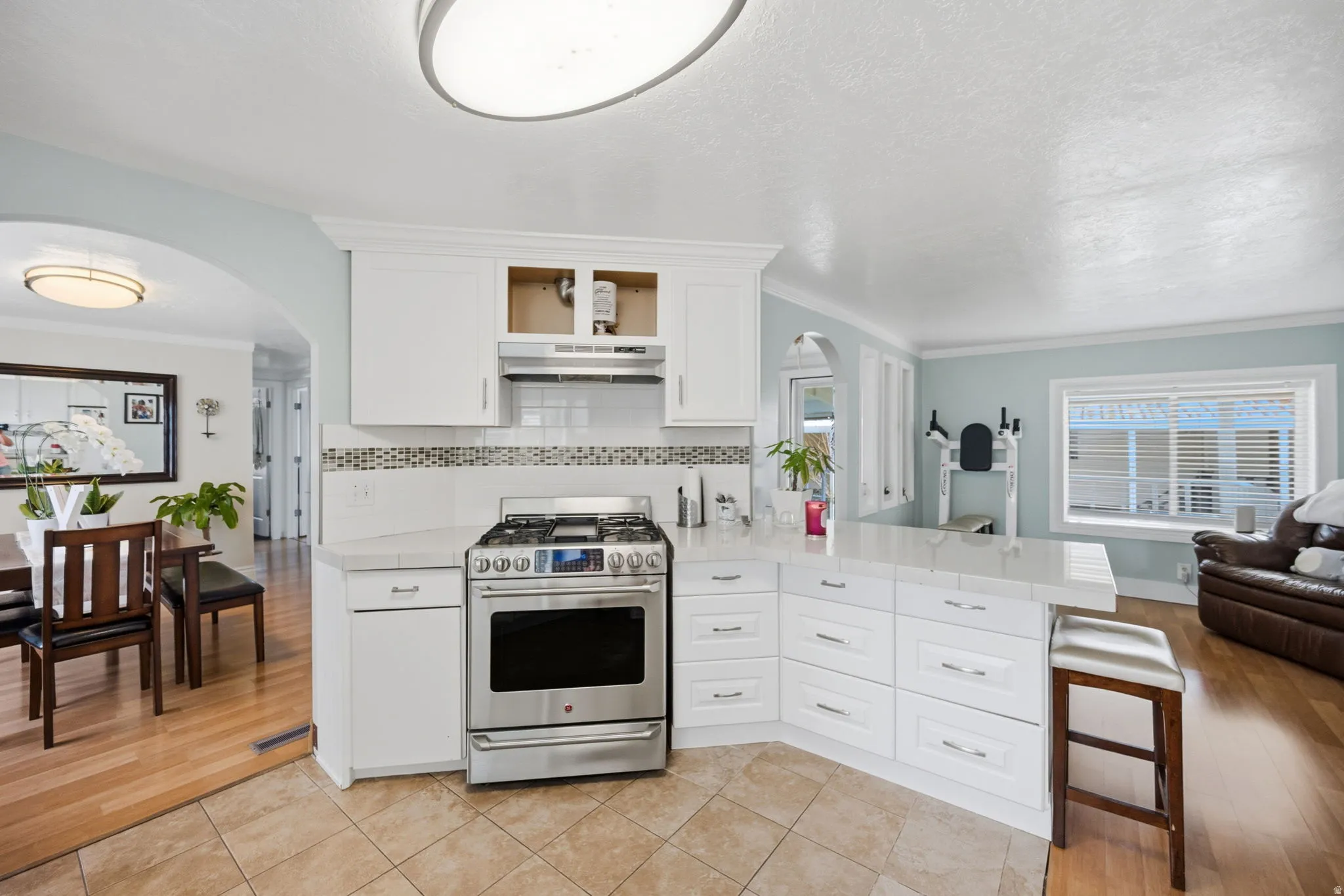 Kitchen featuring arched walkways, stainless steel gas range oven, crown molding, white cabinets, and a peninsula